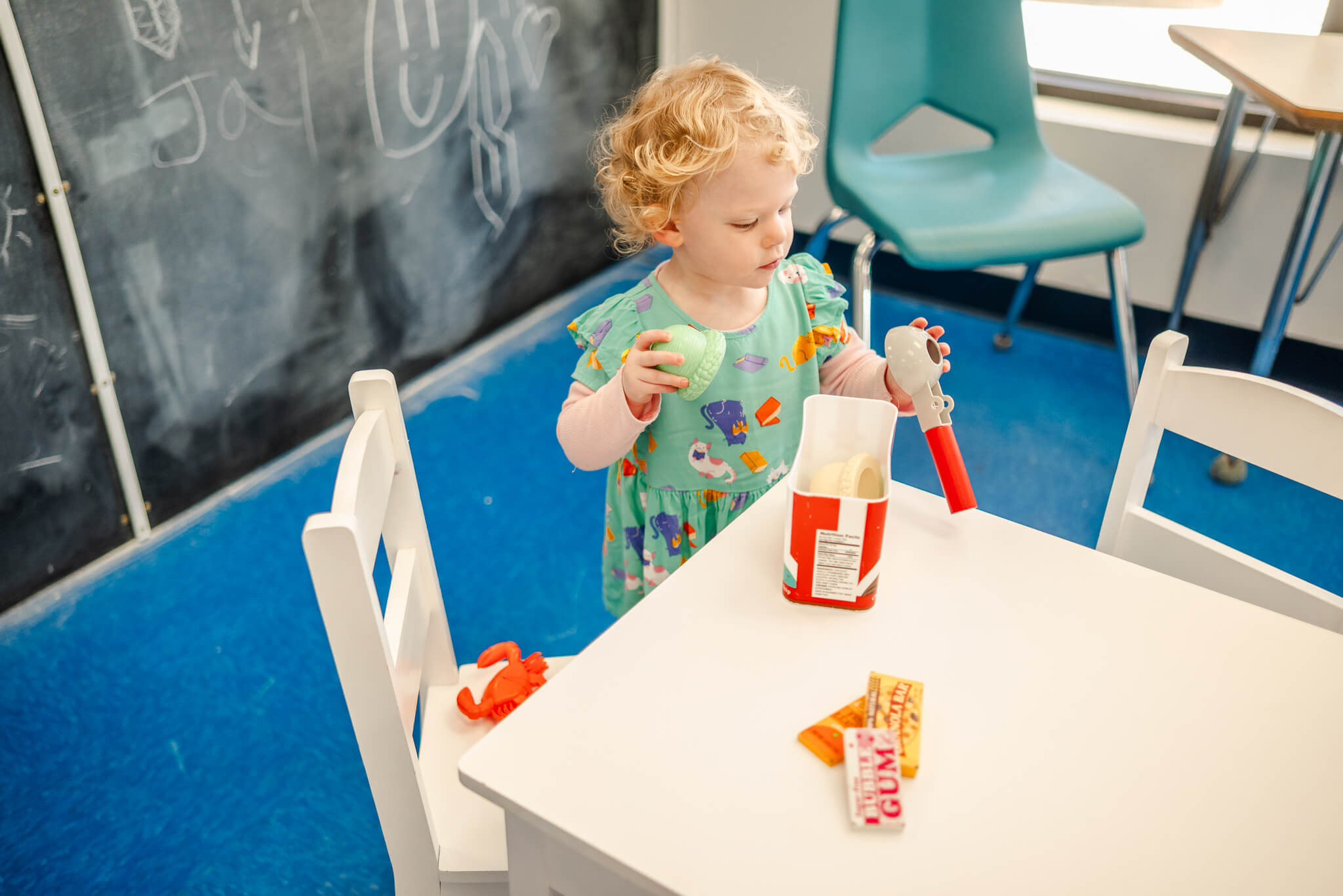 A toddler wearing a teal dress with cats plays at a white table. She is doing the kind of child-centered exploratory play taught at Chesapeake Montessori School.