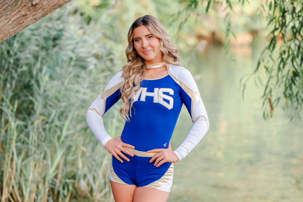 A senior wears her cheer uniform during her Chesapeake senior portraits. She has her hands on her hips and her hair is long and wavy.
