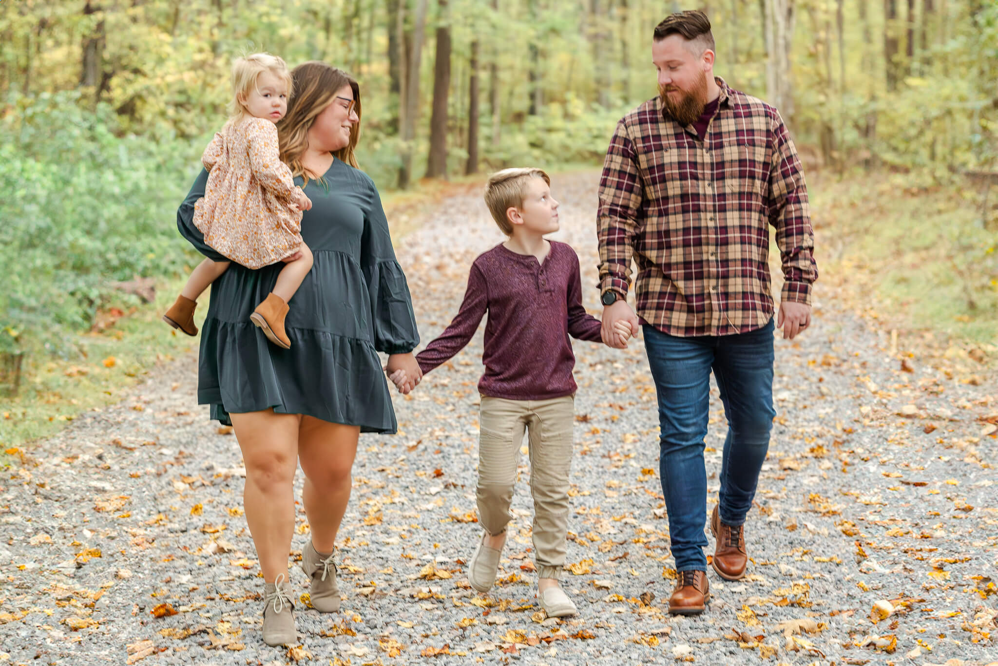 A family of four with a toddler girl and school age son. They are walking on a forest path. The parents use Coastal Childcare to find Virginia Beach babysitters.