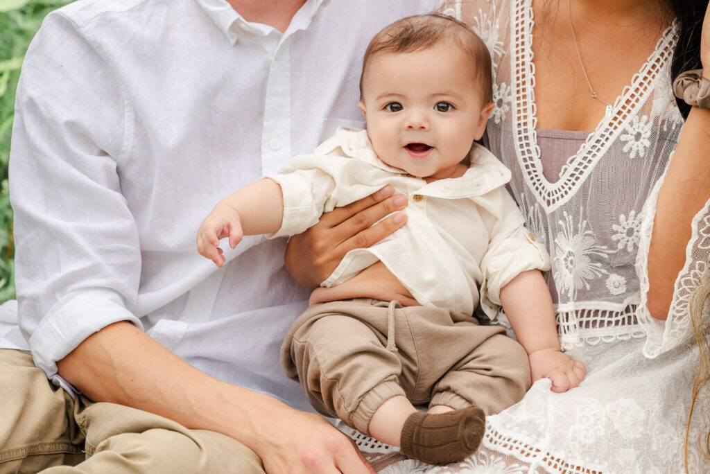 A baby boy wearing and off white shirt and khaki pants sits on his parents' laps. They are also wearing khaki and white. The baby sees a pediatrician in Virginia Beach.