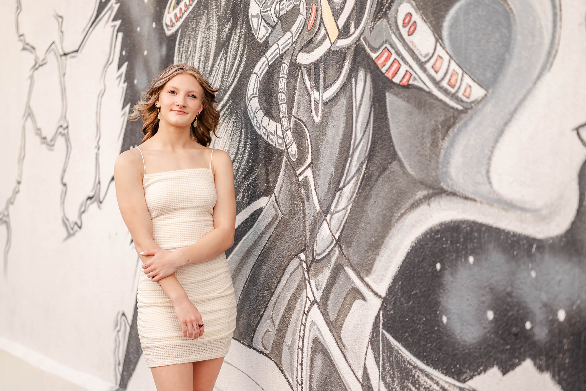 A high school senior in a white dress stands near a black and white mural. She sees a tutor in Virginia Beach.