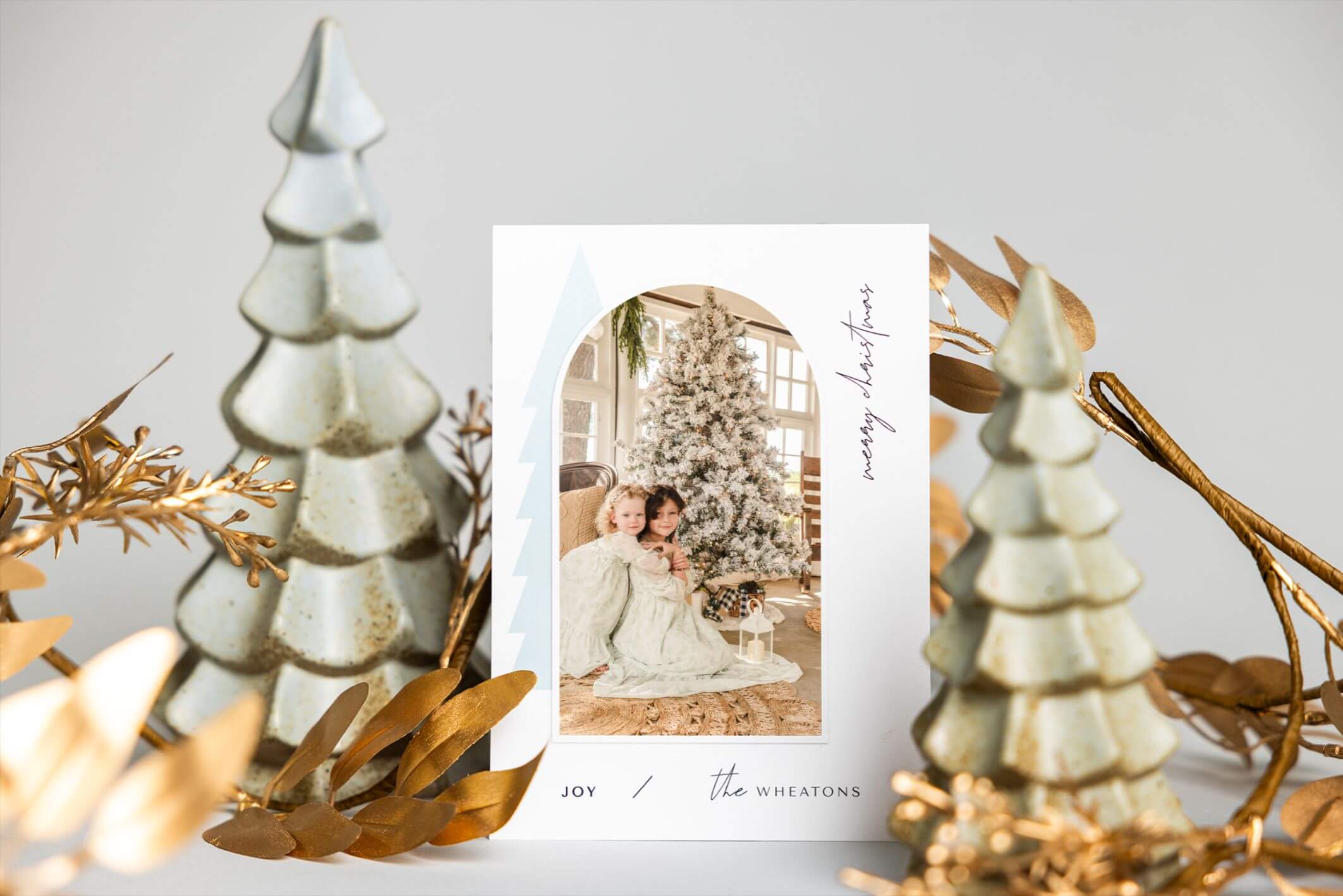 A photo of a Christmas card with two little girls on it, surrounded by Christmas trees. Holiday cards are a great way to turn family photos into gifts.